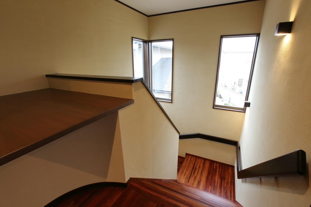 奈良の注文住宅における和モダンな階段空間設計。無垢フローリングと落ち着いた壁面仕上げに、縦長の窓から自然光を取り込み、時間帯によって変化する光と陰影を楽しめる住まい。動線と安全性に配慮しながら、視線の抜けと開放感を生む設計で、日常の移動空間に上質な体験価値をもたらす住宅事例。