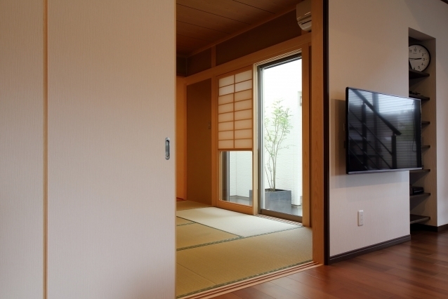 フローリングのLDKと畳敷きの和室が引き戸でゆるやかにつながる和モダン住宅の空間構成。障子越しに中庭の植栽を望み、やわらかな自然光と外部の気配を室内に取り込む設計。開閉により一体空間と個室の両方を実現し、動線と居心地を両立。ホテルライクで上質な暮らしを求める方に向けた和室のある住まいの一例。