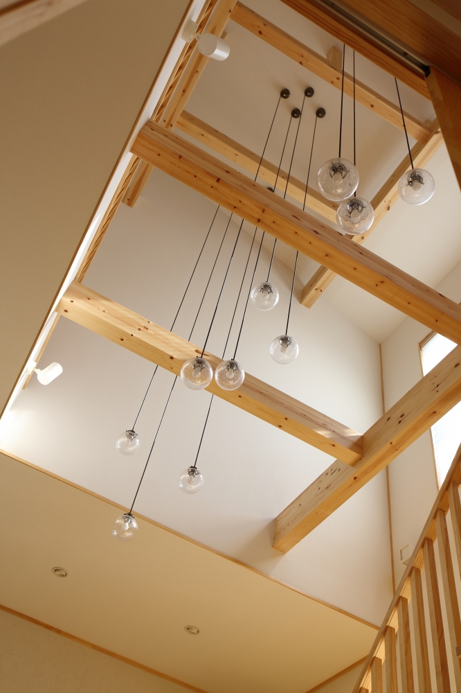 吹き抜けのある和モダン住宅の室内空間。無垢材の梁と柱を現しにした木構造と、高天井から吊り下げられたガラスペンダント照明が印象的な設計。自然光を取り込む開放的な空間構成により、明るさと奥行き、上質な陰影を両立。奈良の注文住宅・高級住宅において、構造美とインテリアデザインを融合させたホテルライクで洗練された住まいの一例。