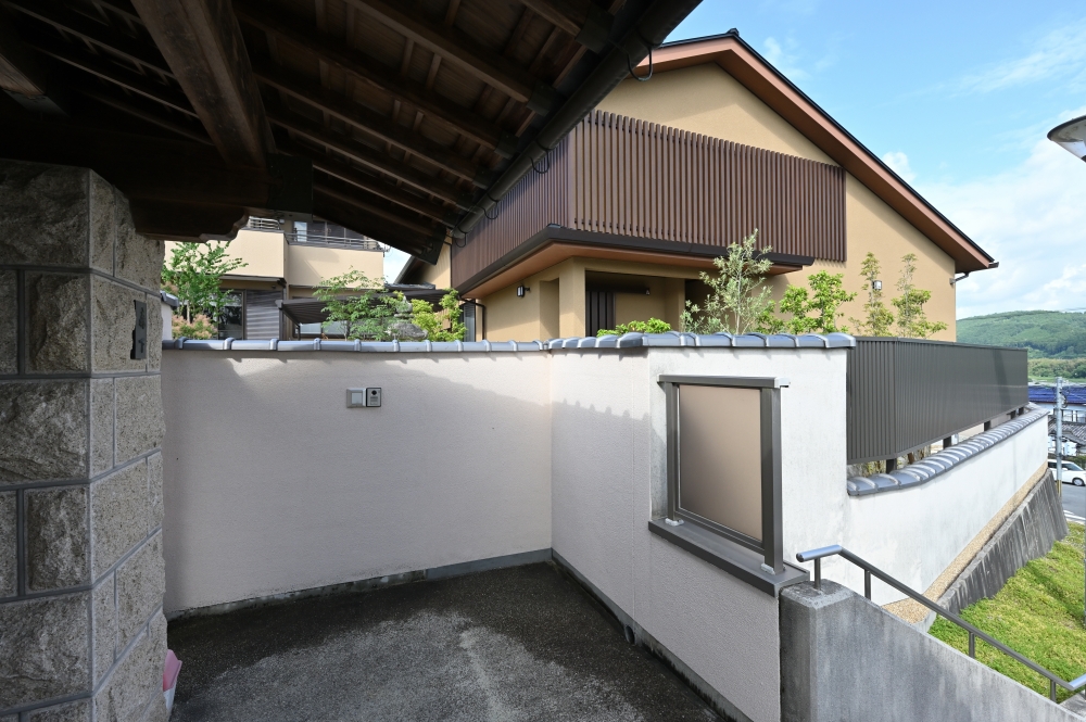 奈良県の和モダン住宅の外観と外構。塀に囲まれたプライベート空間と、木格子のファサードが調和する住まい。深い軒と落ち着いた外壁色が陰影を生み、外からの視線を遮りながら内側に静けさと上質な暮らしを実現した注文住宅事例。