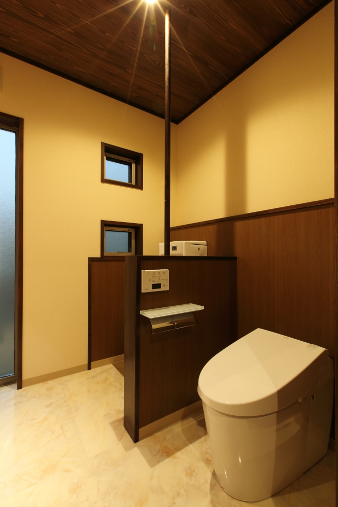 奈良の注文住宅における一階トイレ空間の設計事例。木質パネルで仕切られた落ち着きのある空間構成に、手洗い機能と一体化した設計で使い勝手を向上。無垢調の天井と間接的な照明計画により、ホテルライクで上質な和モダンのトイレ空間を実現した住宅。