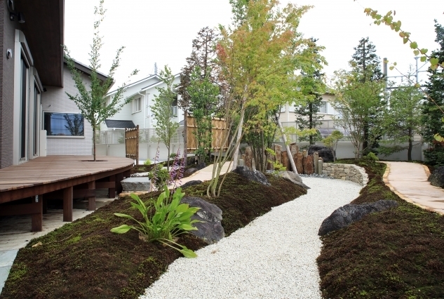 奈良県の建築家設計による高級和モダン住宅の庭とウッドデッキ空間。 曲線のウッドデッキと白砂の園路、苔や自然石、植栽が調和し、外と内をつなぐ回遊性のある外構デザインを実現した注文住宅。