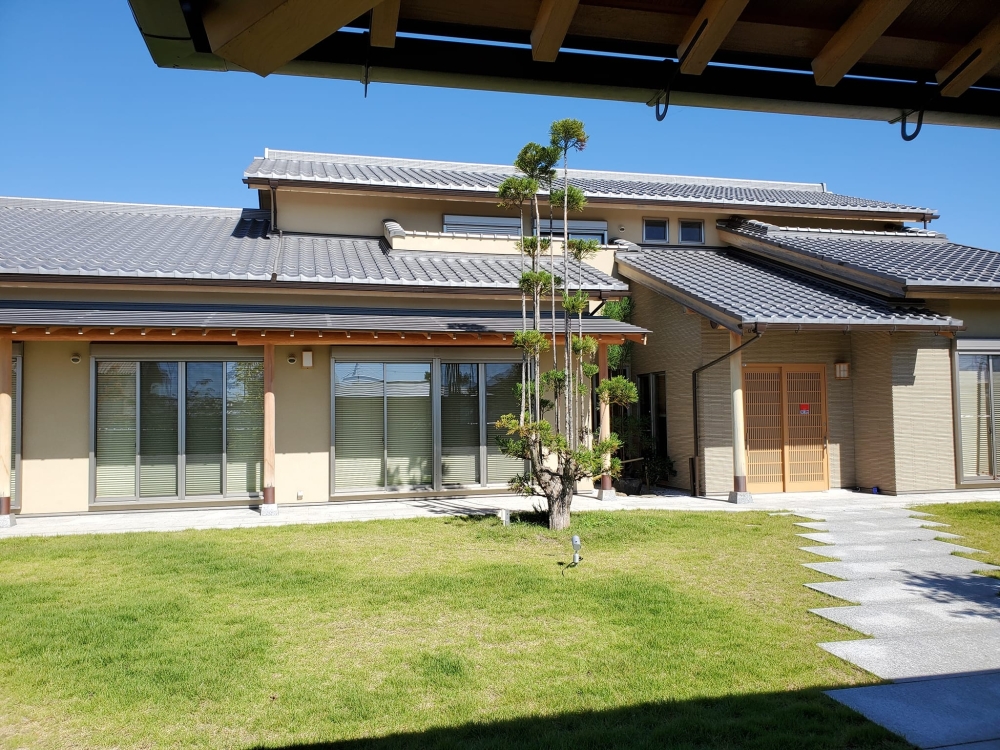 奈良県のやまぐち建築設計室が設計した数寄屋風和モダン住宅の庭側外観。芝生の庭と一体化した開放的な設計で、深い軒と縁側空間が内外を緩やかにつなぐ。瓦屋根と木造架構の美しさ、中央に配された植栽が空間の軸となり、光と陰影の移ろいを楽しめる高級注文住宅の設計事例。奈良で上質な暮らしを叶える和風住宅。