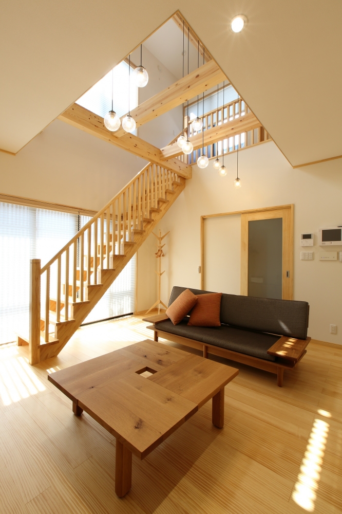 和モダン住宅の吹き抜けリビング空間。無垢材の梁とリビング階段が美しく構成され、ペンダント照明が空間にリズムと奥行きを与えるデザイン。大きな窓から自然光が差し込み、明るさと開放感を両立。奈良の注文住宅における、構造美と居住性を融合したホテルライクで上質な住まいの設計事例。