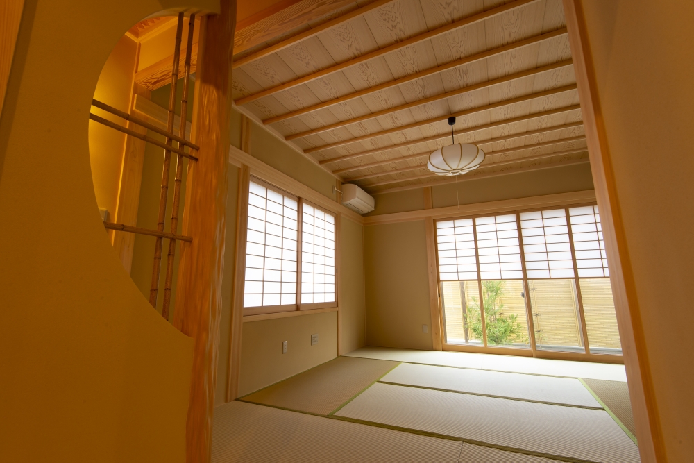 奈良県のやまぐち建築設計室が設計した数寄屋風和モダン住宅の和室空間。障子からやわらかな自然光を取り込み、畳と木組み天井、竹意匠を取り入れた意匠が調和する設計。円形開口の意匠壁と地窓から坪庭を望む構成により、内と外が穏やかにつながる落ち着きある住空間を実現。高級注文住宅・和風住宅・和モダン住宅の設計実例。