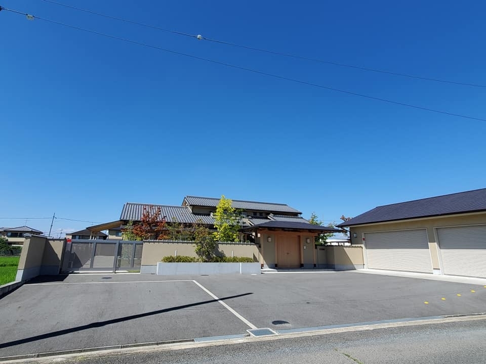奈良県のやまぐち建築設計室が手がけた和モダン住宅の外観。重厚な瓦屋根と深い軒、塀に囲われたプライベート性の高い外構計画が特徴で、門から玄関へと続くアプローチに植栽と陰影が美しく調和。独立型ガレージを備え、動線と景観を両立した高級注文住宅の設計事例。