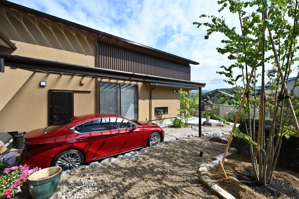 奈良県の和モダン注文住宅の外観。深い軒と木格子が陰影を生むファサードに、庭と連続するアプローチとカーポートを計画。自然素材と外構デザインが調和し、内外の境界を曖昧にする設計により、静けさと上質な暮らしを実現した住宅事例。