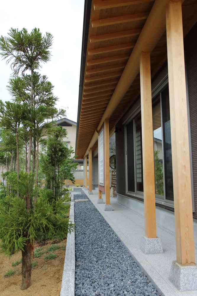 奈良県の建築家による高級和モダン住宅の外観。 深い軒と無垢の木柱が連続する縁側空間に、石張りの基壇と砂利敷き、植栽が調和し、光と陰影が美しく移ろう注文住宅の外構デザイン。