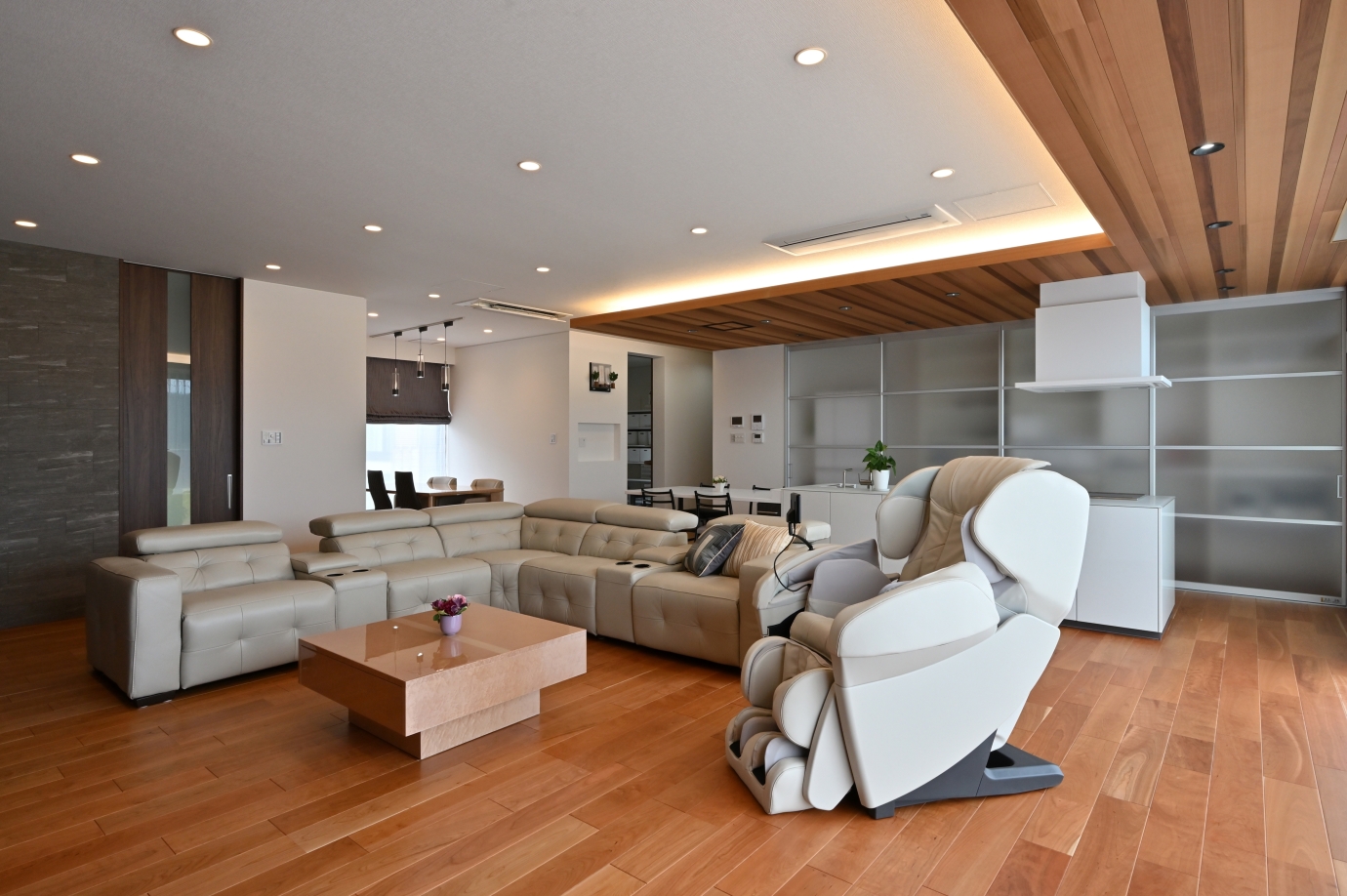 建築家が設計した奈良の和モダン注文住宅のLDK。木目天井と間接照明が空間に奥行きを生み、ゆったりとしたソファ配置と回遊性のあるキッチンが上質でホテルライクな暮らしを演出する。